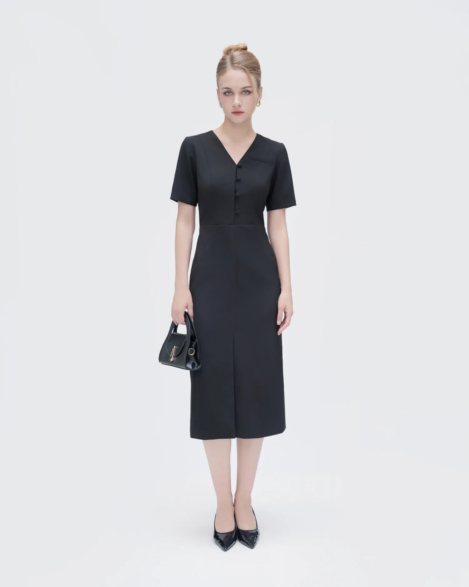 Woman in elegant ROSIE HONG black dress holding a handbag, standing against a white background.