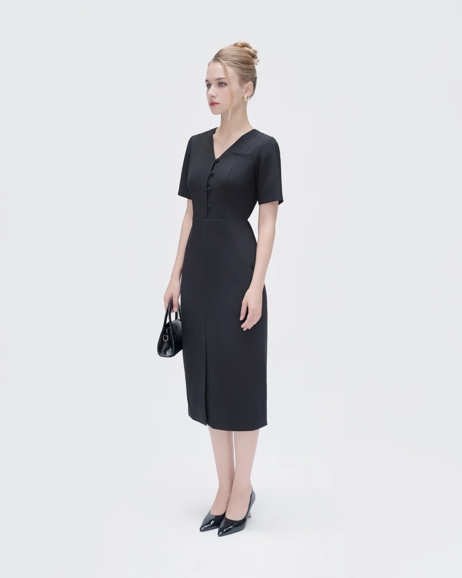 Elegant woman in black dress holding a handbag, standing against a white background.