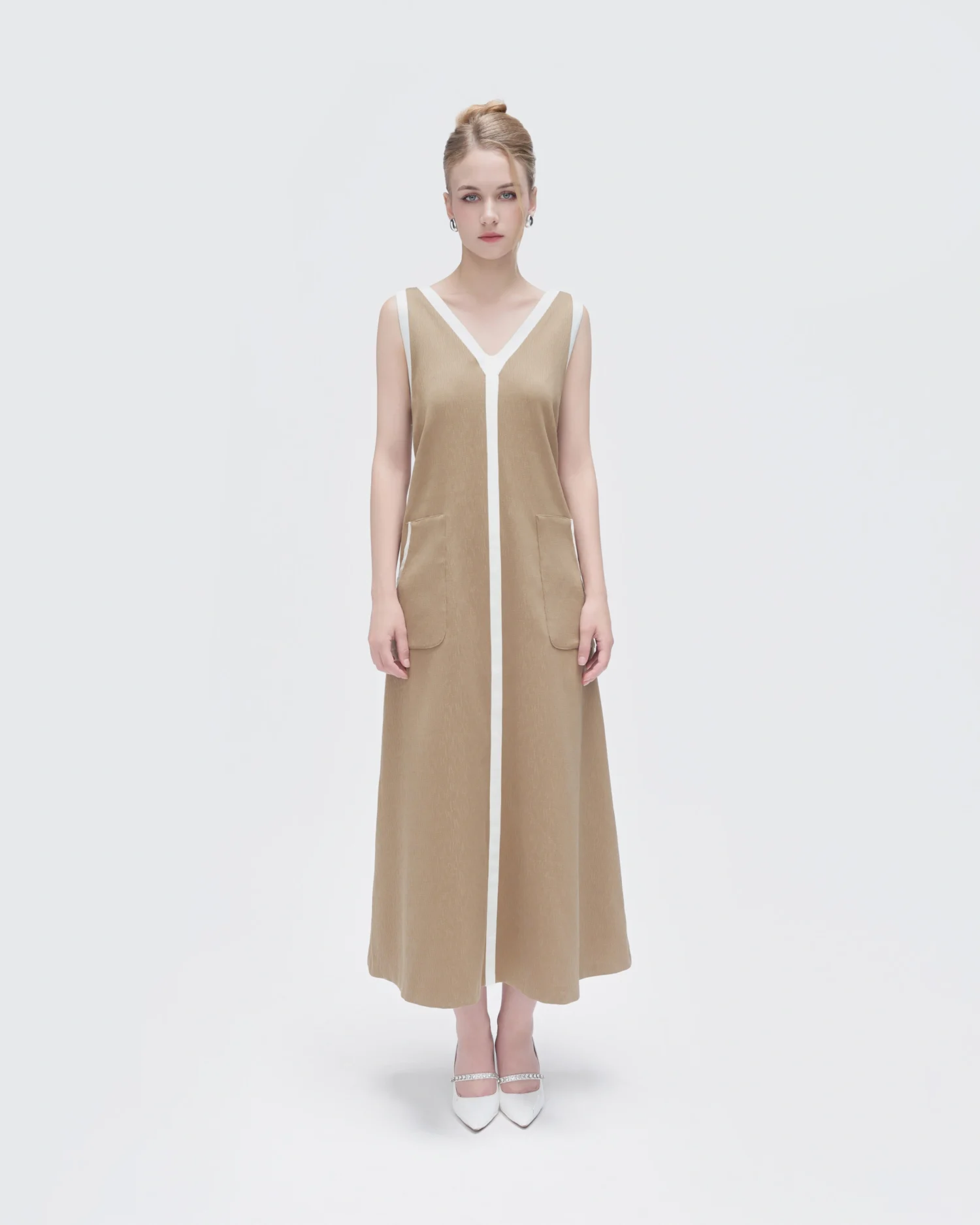 Woman in sleeveless beige dress with white trim, standing on white background. Fashion photography.