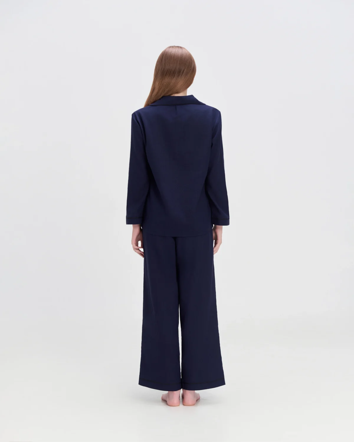 Rear view of a women in a navy two-piece loungewear set, standing barefoot against a white background.