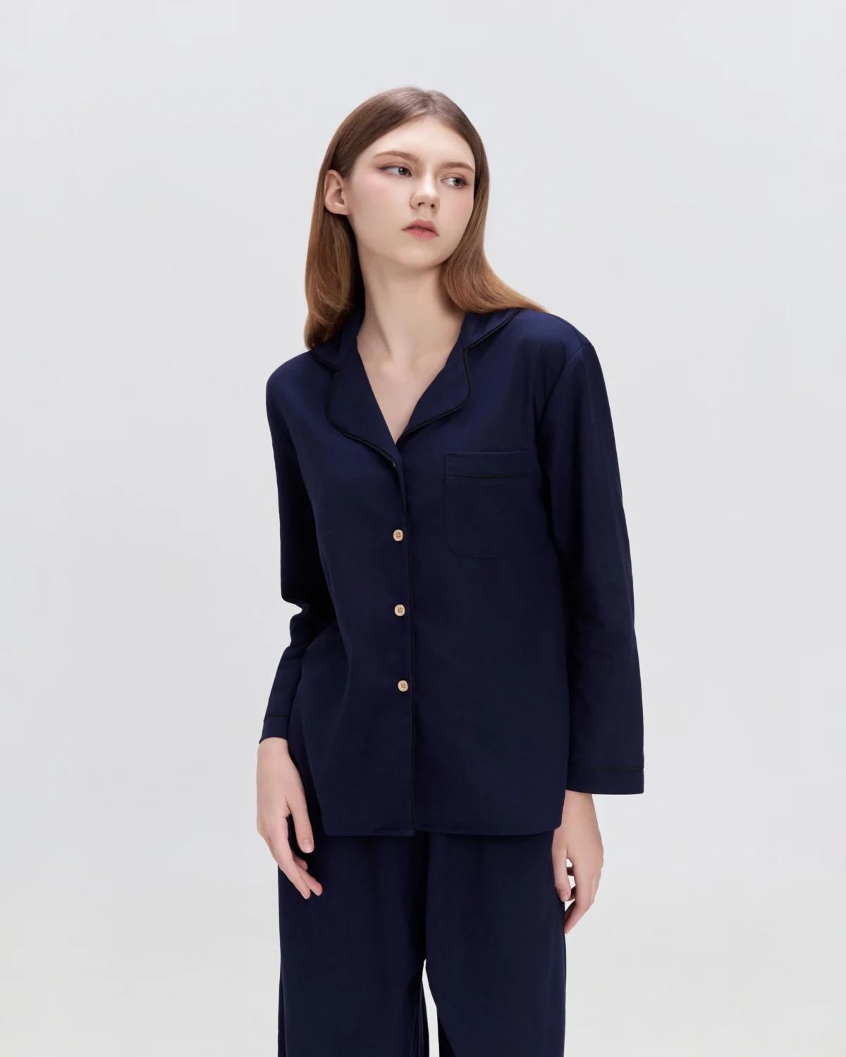 Woman in navy button-up pajama set with a minimalist backdrop, showcasing casual sleepwear fashion.