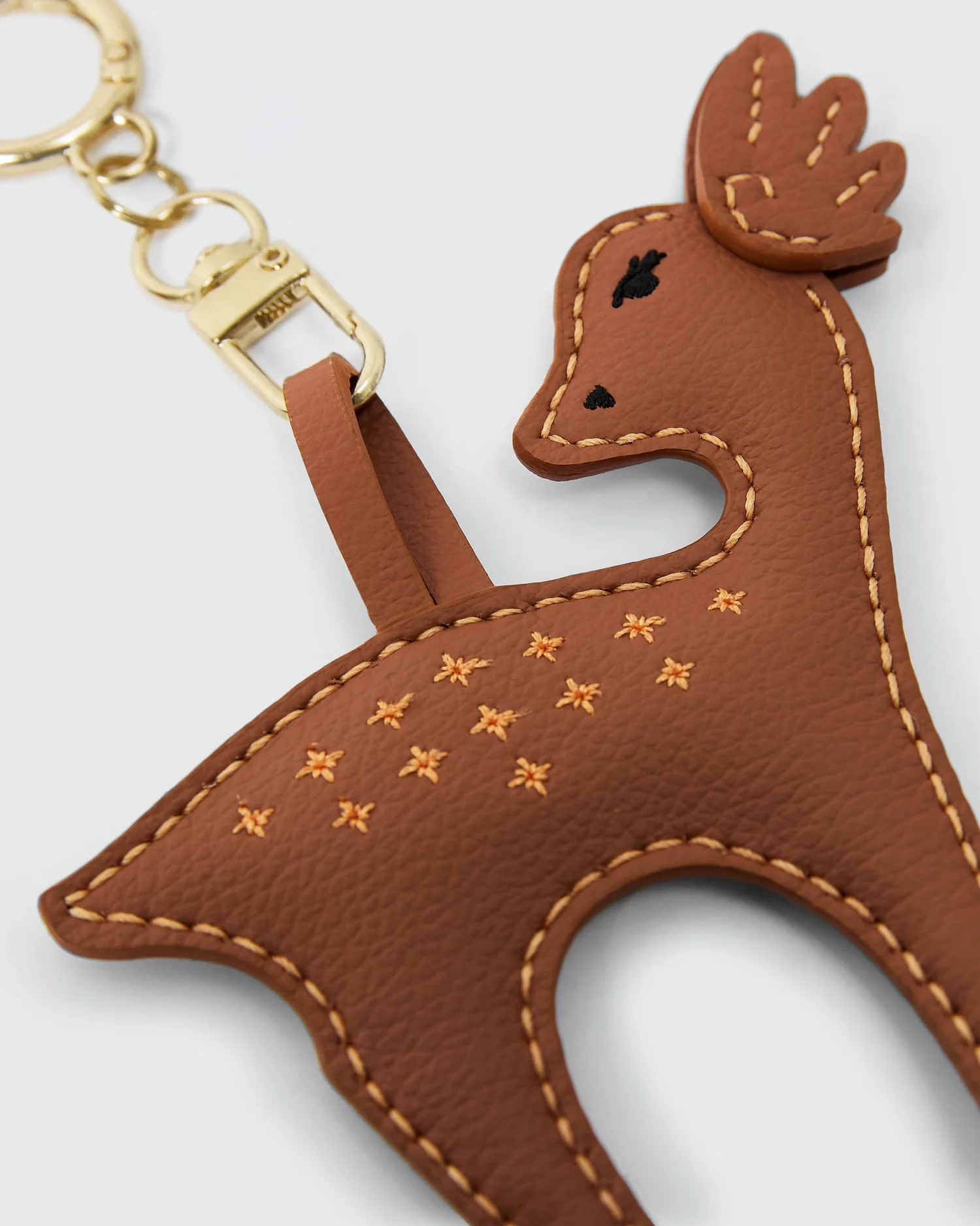 Brown vegan leather reindeer keychain with yellow stitching detail and gold clasp on a light background.