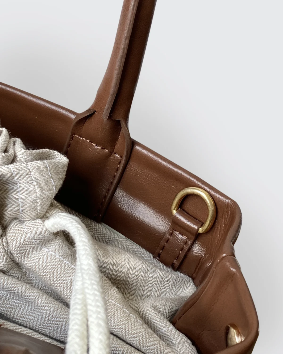 Close-up of brown leather handbag with beige fabric lining and metal ring detail.