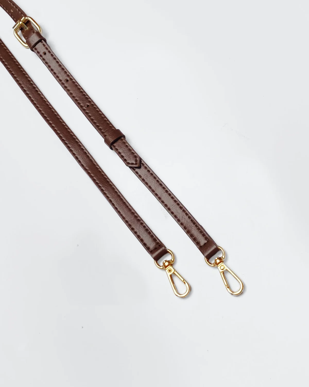 Brown leather handbag straps with gold clasps on a white background, showcasing elegant accessory design.