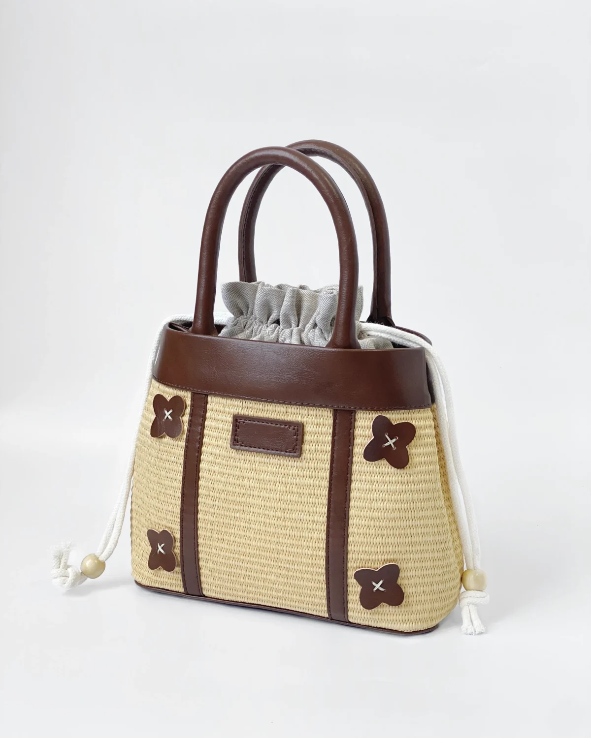 Stylish straw tote bag with brown leather accents and floral details, perfect for a chic summer look.