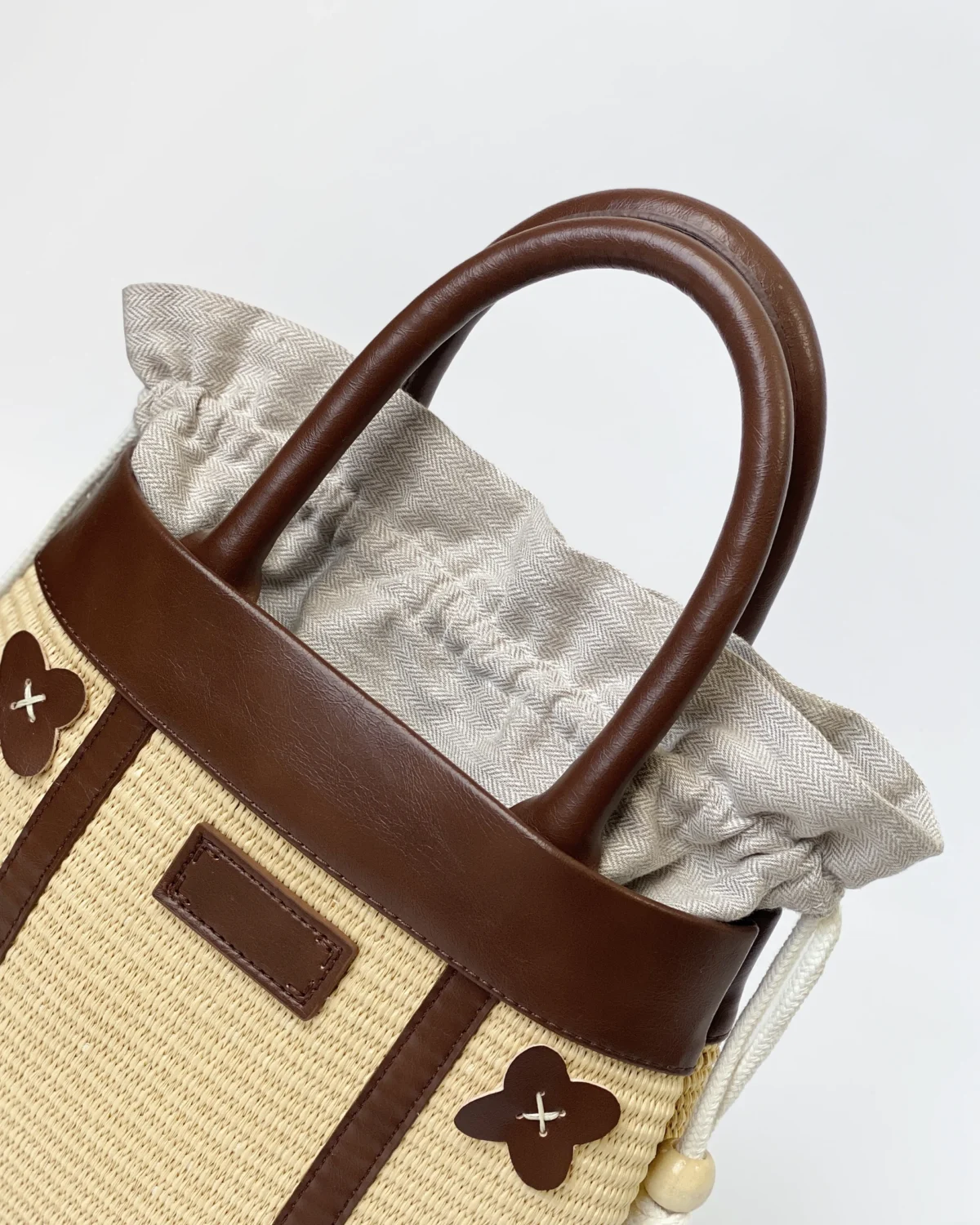 Stylish beige and brown handbag with leather handles and floral accents on a white background.