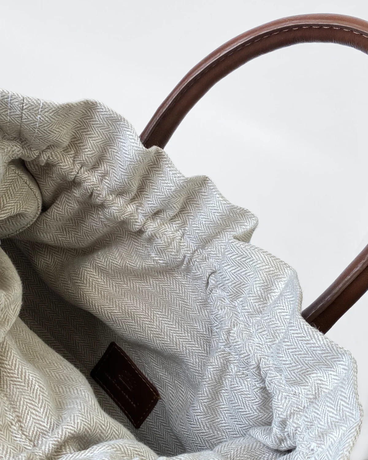 Close-up of a fabric tote bag with herringbone pattern and leather handles, showcasing interior design.