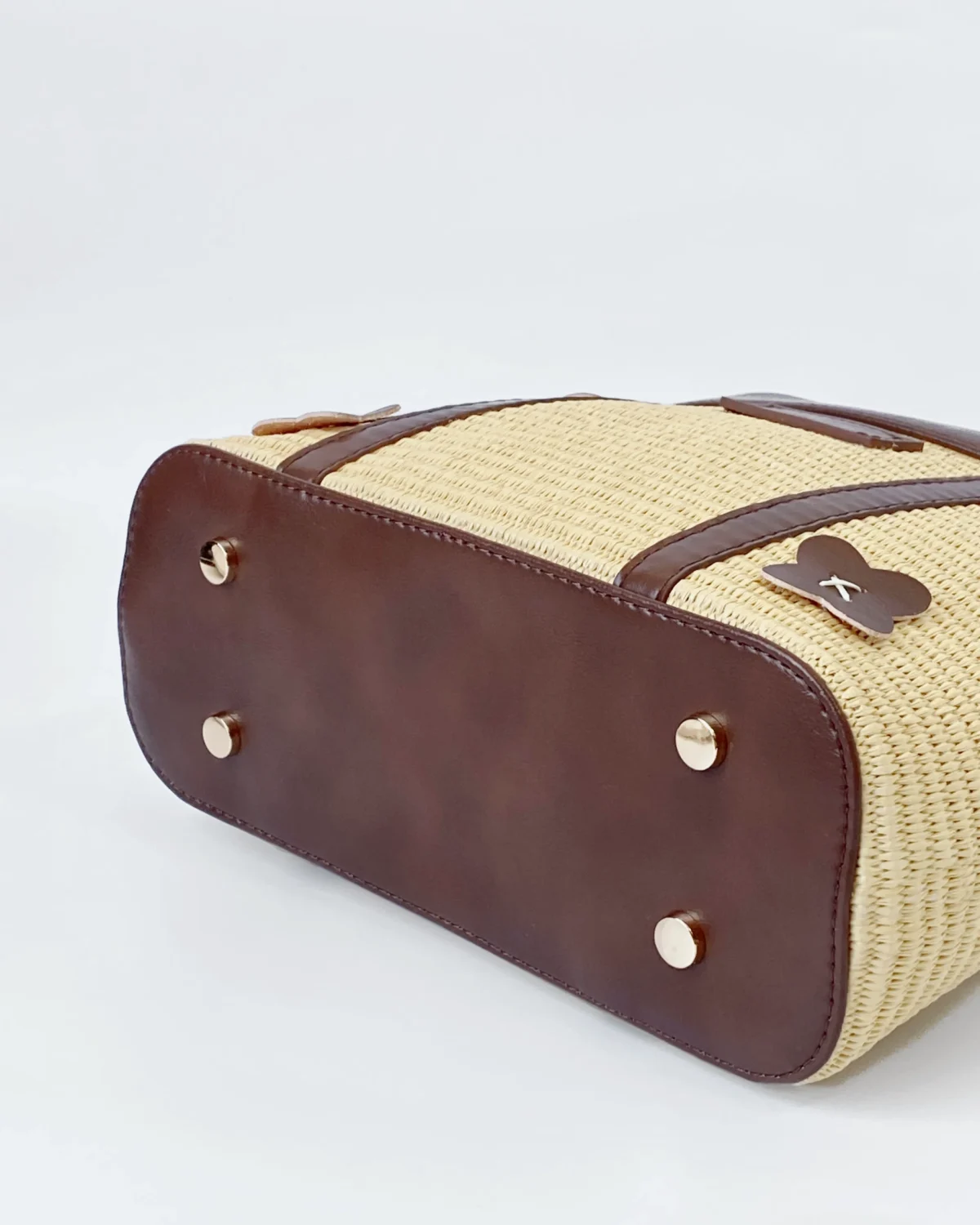Bottom view of a stylish woven ROSIE HONG handbag with dark brown leather accents and metal feet on a white background.