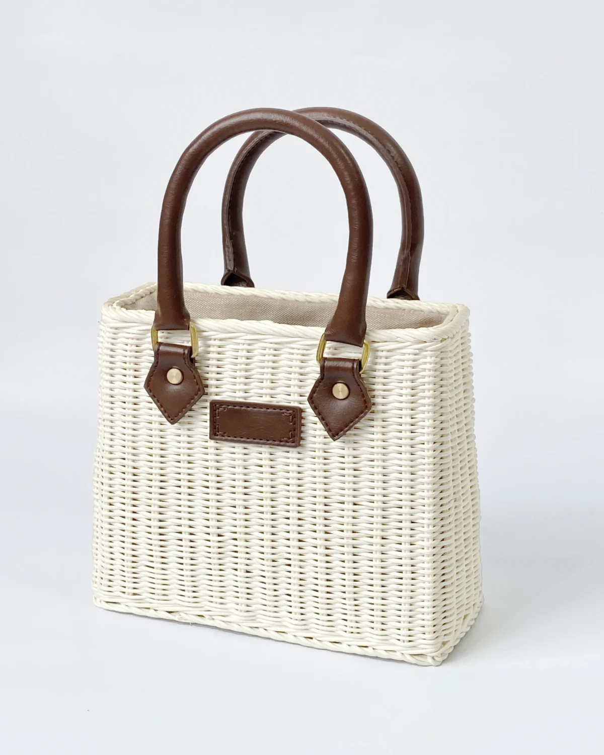 White woven handbag with brown leather handles and accents, perfect for a stylish summer or casual outing.