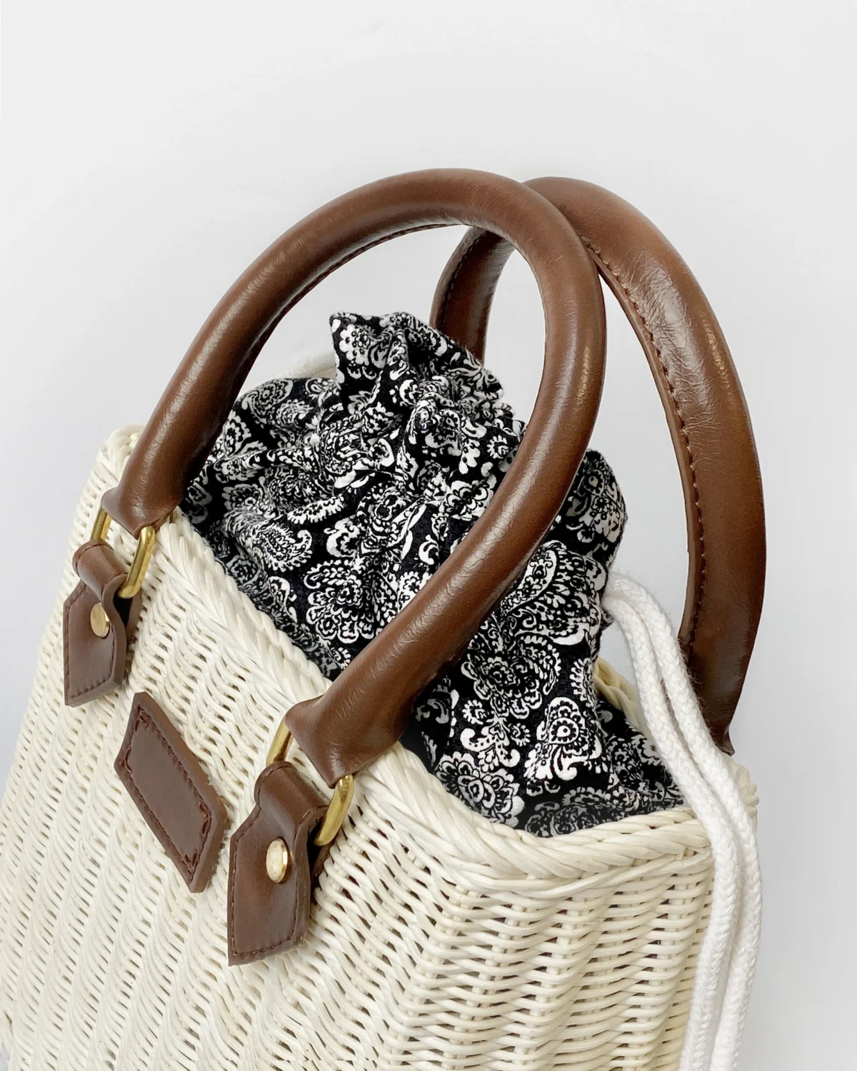 Woven ROSIE HONG handbag with brown leather handles and a black and white floral fabric lining. Stylish and elegant accessory.