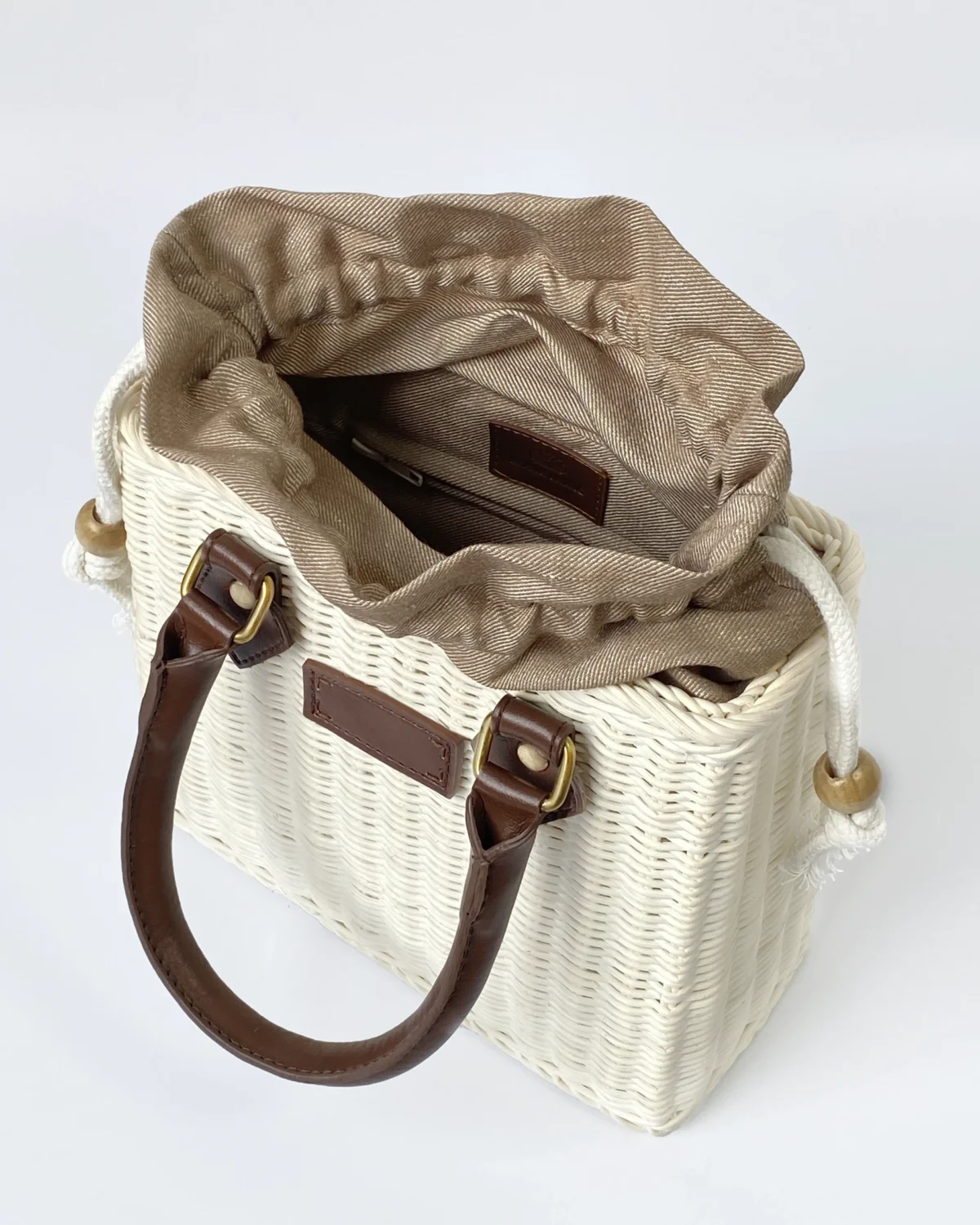 Elegant wicker handbag with brown leather handles and beige fabric lining. Ideal for summer outings and stylish looks.