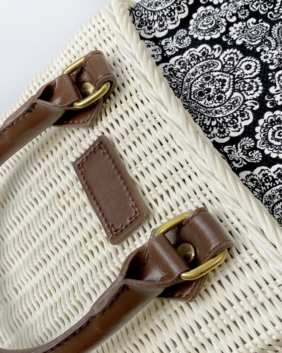 Close-up of woven bag with brown leather handles and a black paisley fabric lining, highlighting detailed craftsmanship.
