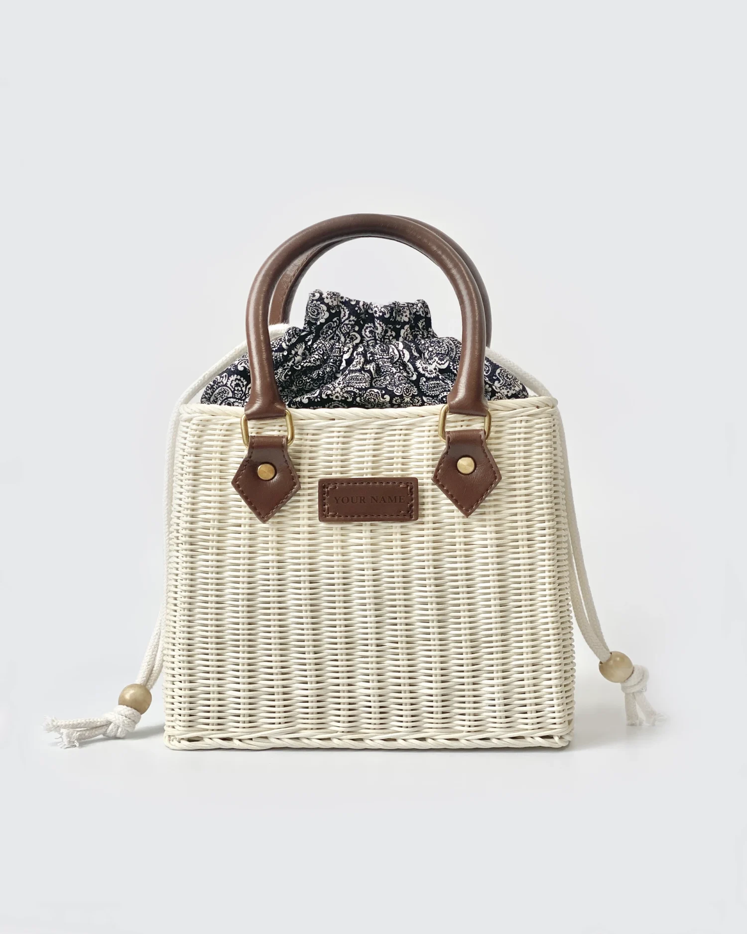 Wicker handbag with leather handles and paisley fabric lining, featuring a custom nameplate for personalized style.