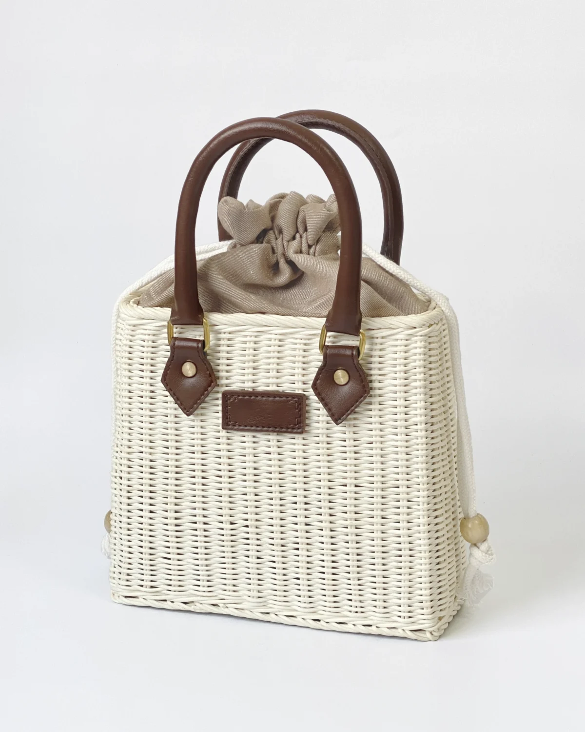 Stylish woven handbag with brown leather handles and beige fabric drawstring. Perfect for summer outings or casual wear.