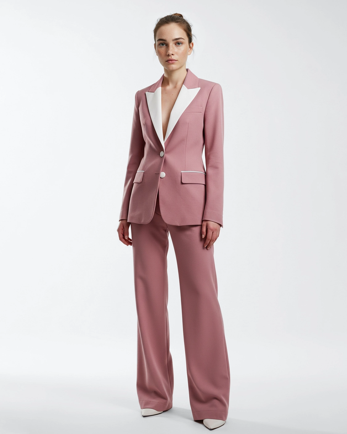 Woman in a stylish pink suit with white lapels, posing confidently against a white background. Fashion and elegance.