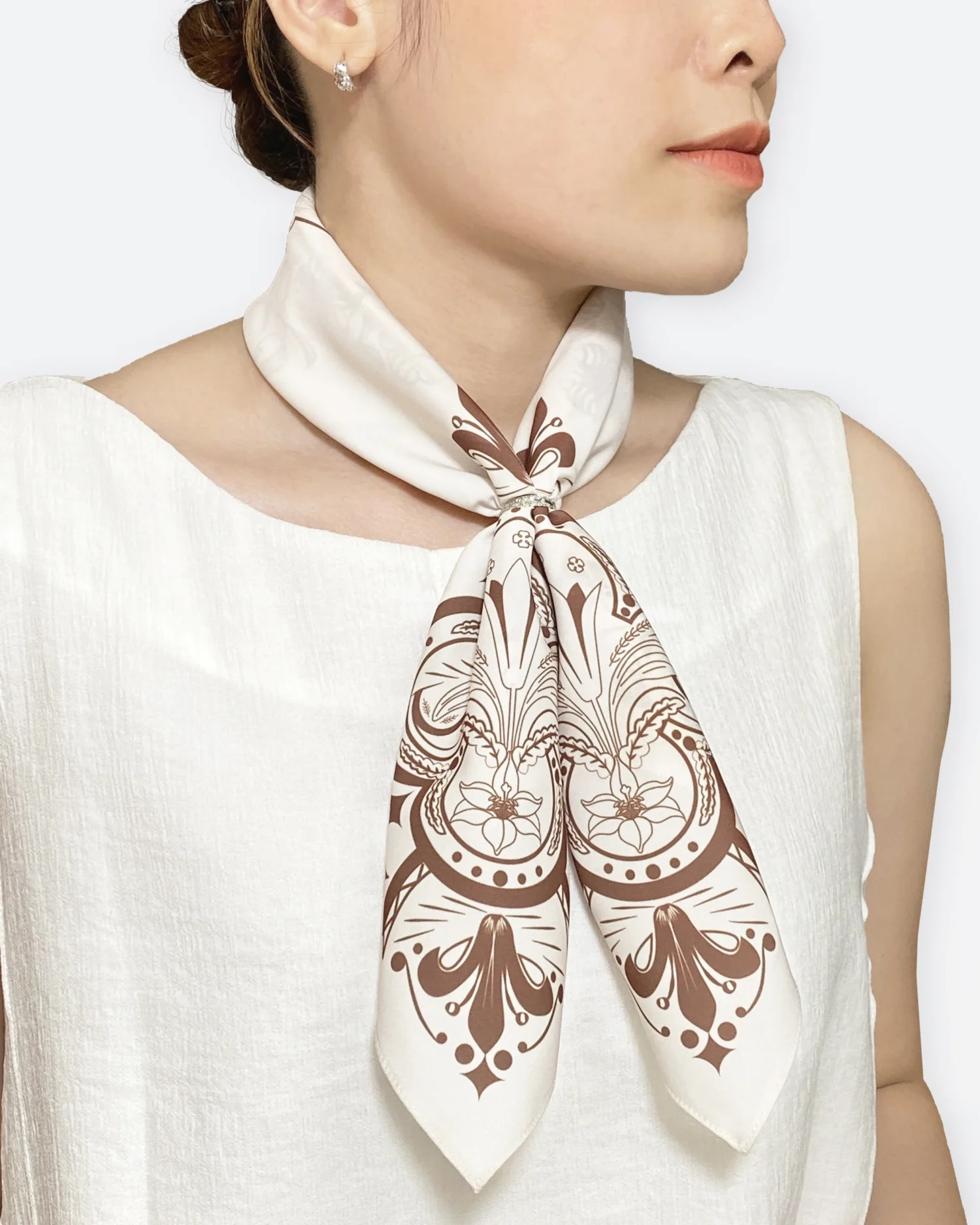 Elegant woman wearing a decorative brown and white scarf, paired with a sleeveless white top.