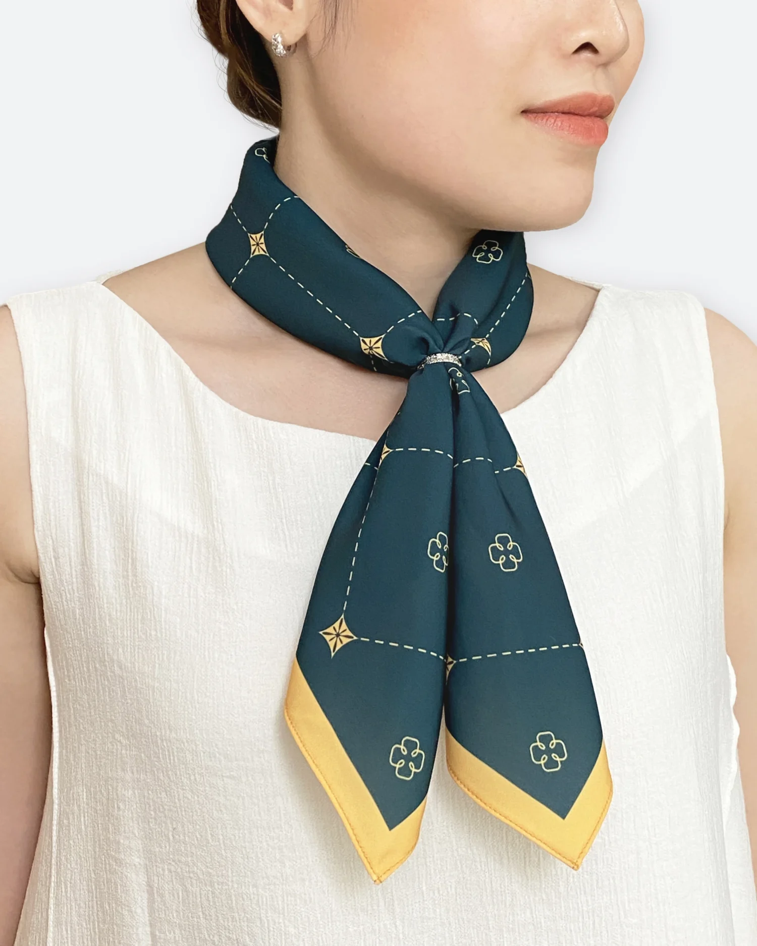 Woman wearing a patterned navy and gold neck scarf, paired with a white sleeveless top.