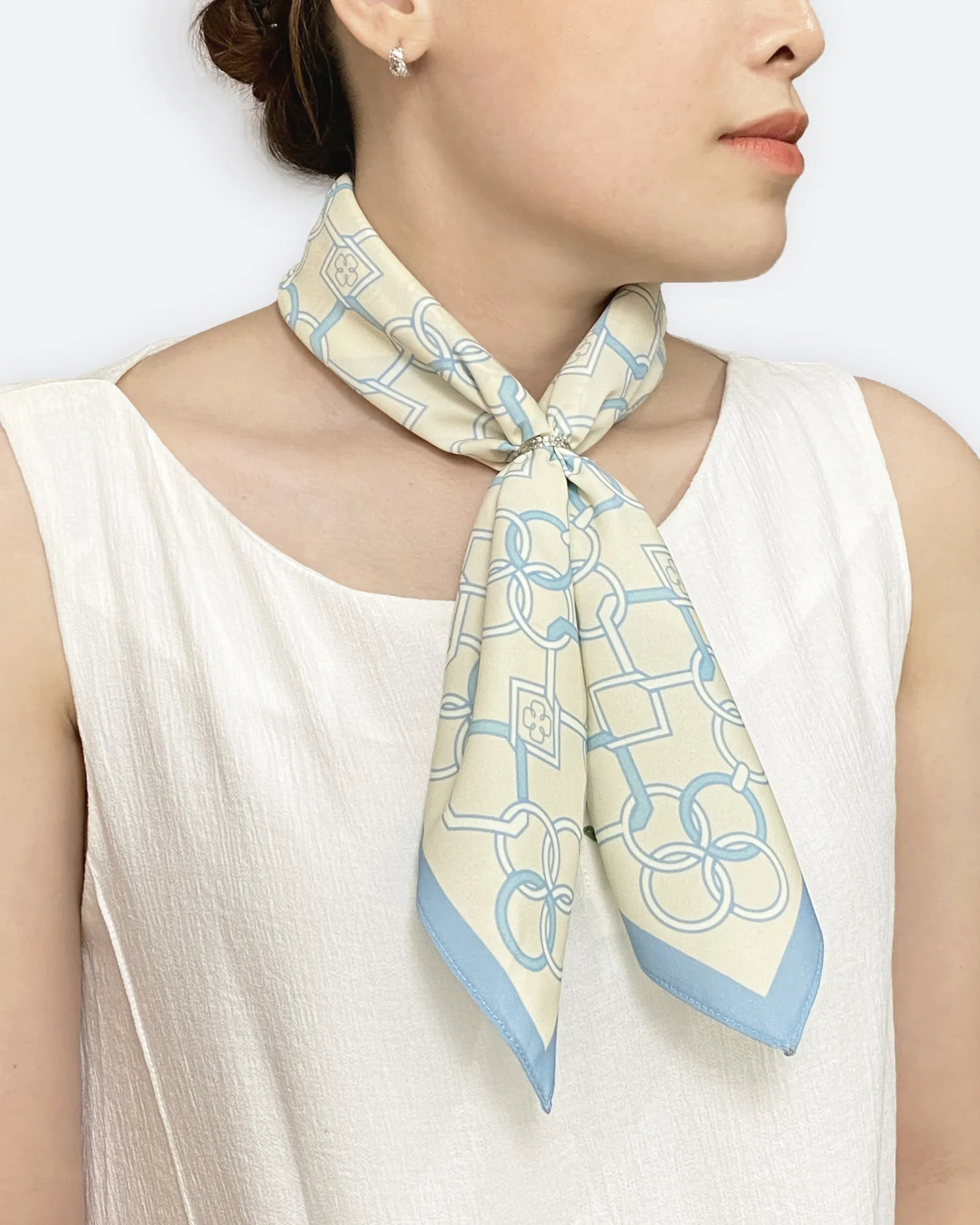 Elegant cream and blue patterned silk scarf tied around woman's neck with white top.