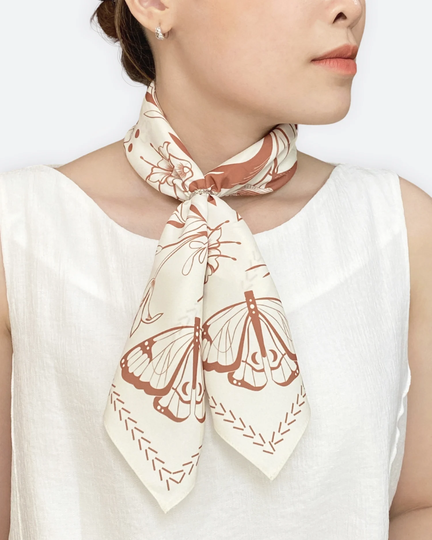 Silk scarf with floral and butterfly designs worn around a woman's neck, paired with a white top.