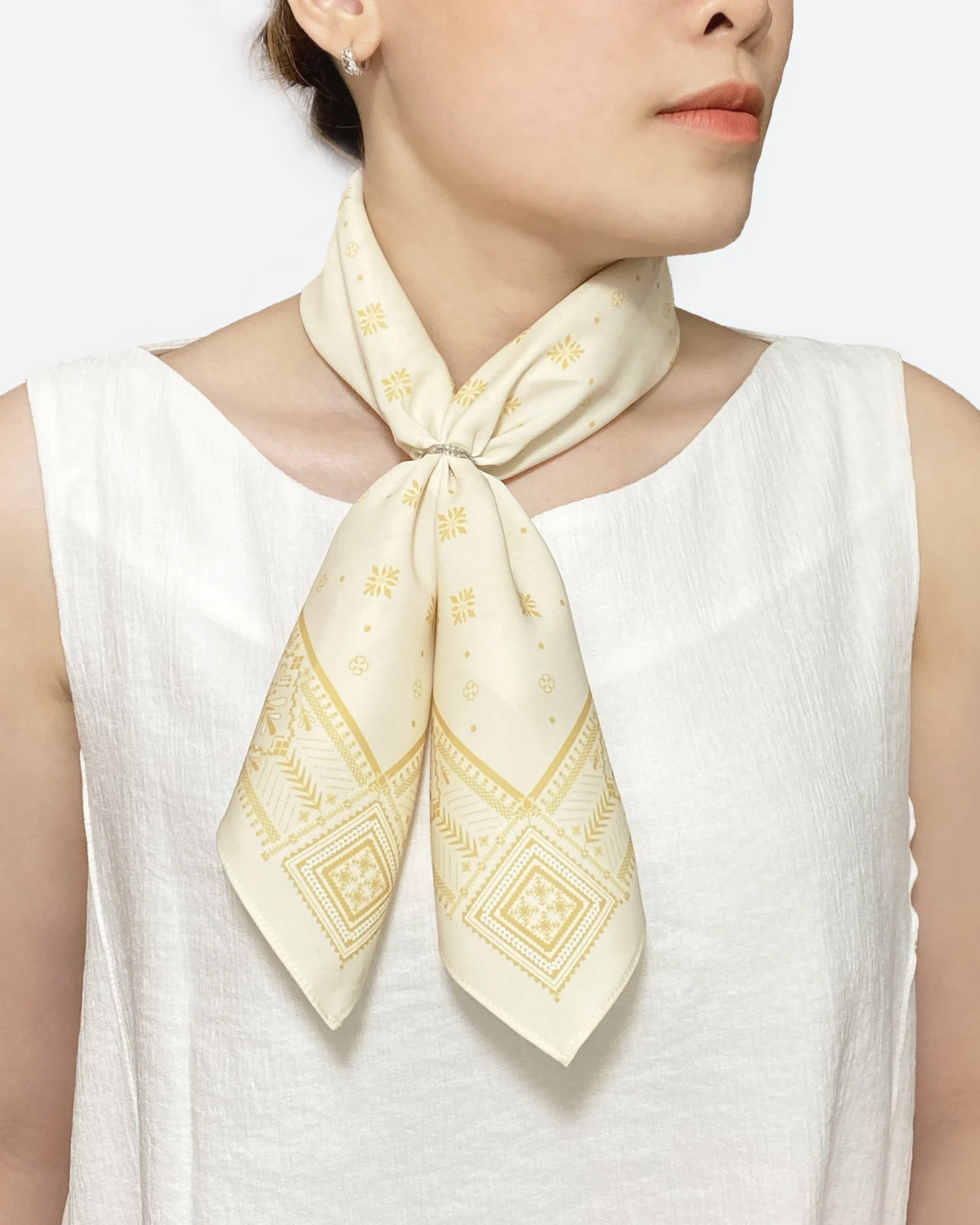 Elegant white and gold-patterned scarf tied stylishly around woman's neck, complementing her white sleeveless top.
