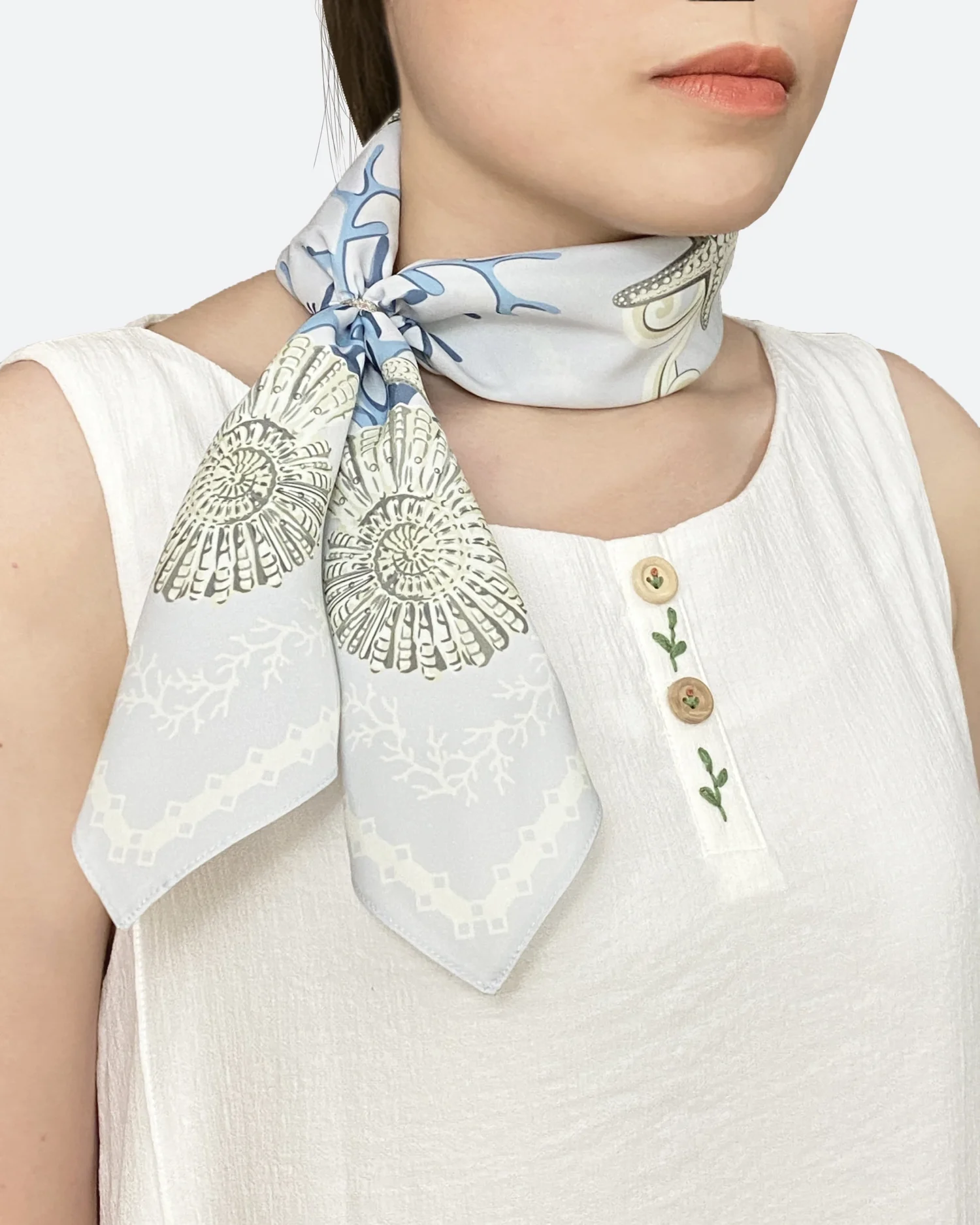 Silk scarf with intricate floral pattern tied around neck, worn over a sleeveless white blouse.