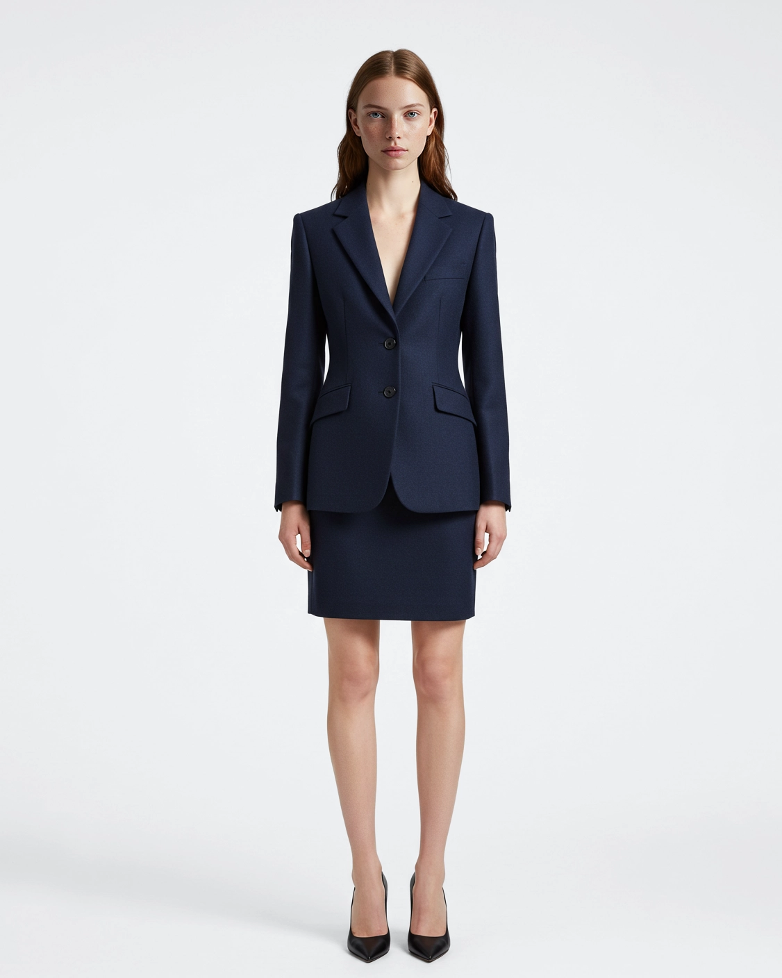 Woman in navy blue business suit with skirt, standing confidently against plain background.