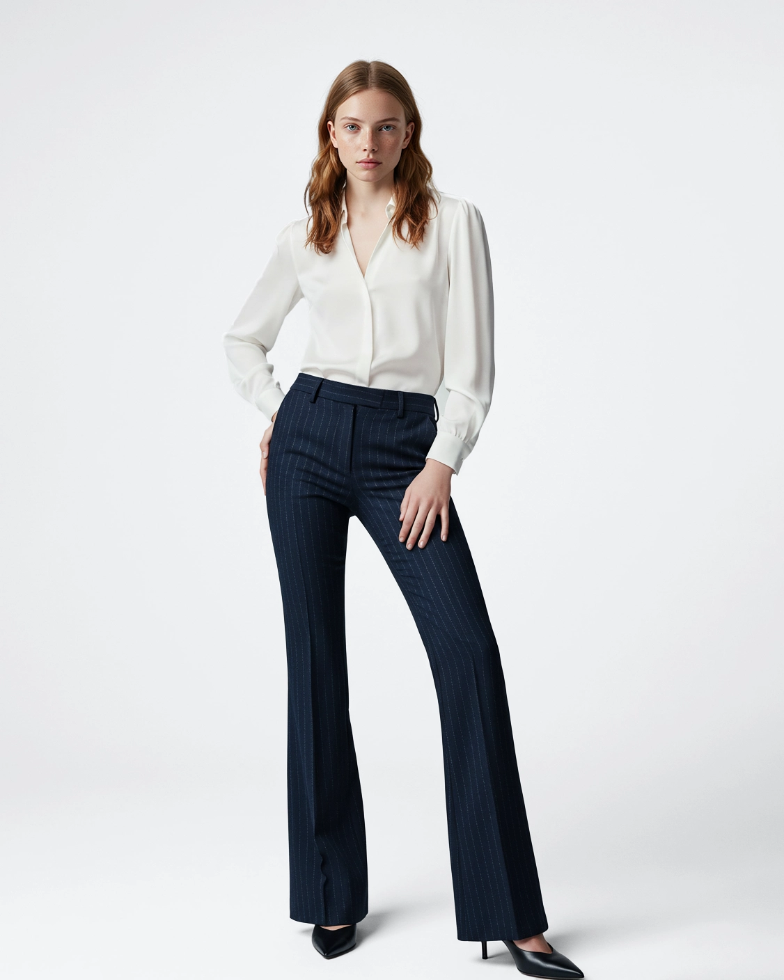 Woman in stylish white blouse and pinstripe pants, posing confidently, on a white background.