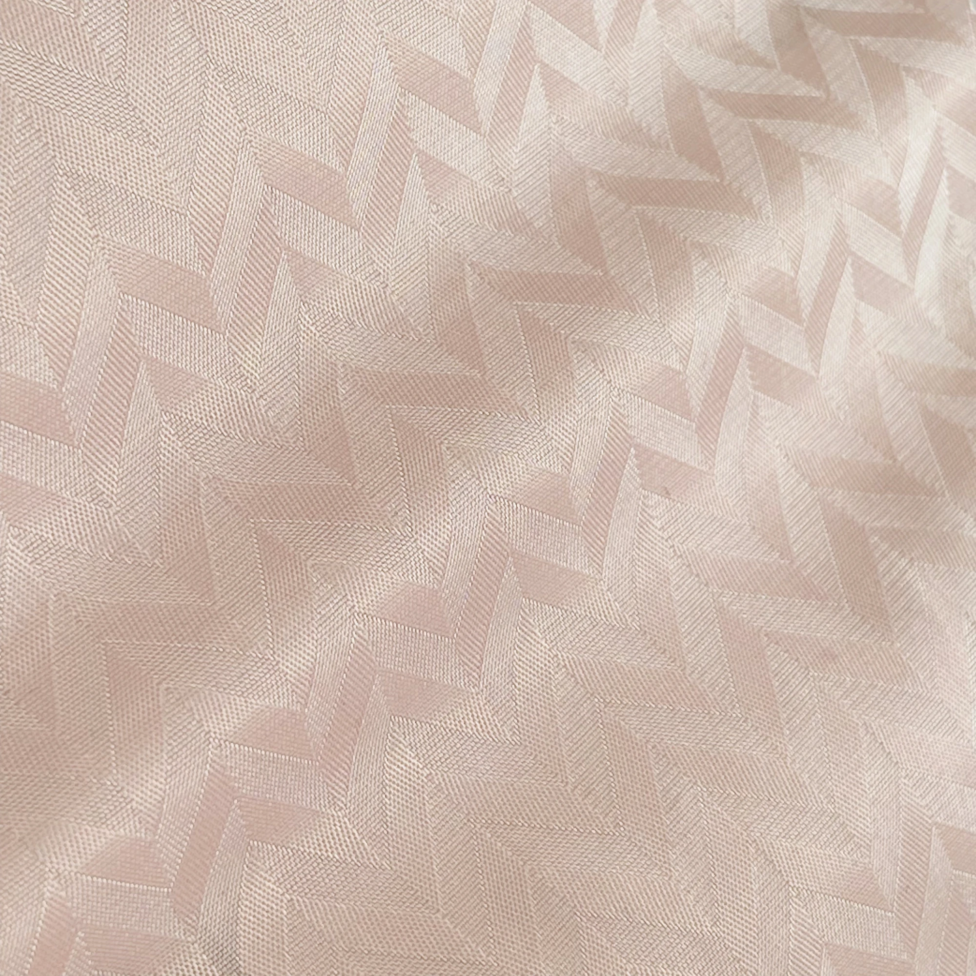 Close-up of soft herringbone fabric in light beige, displaying intricate woven texture and subtle geometric pattern.