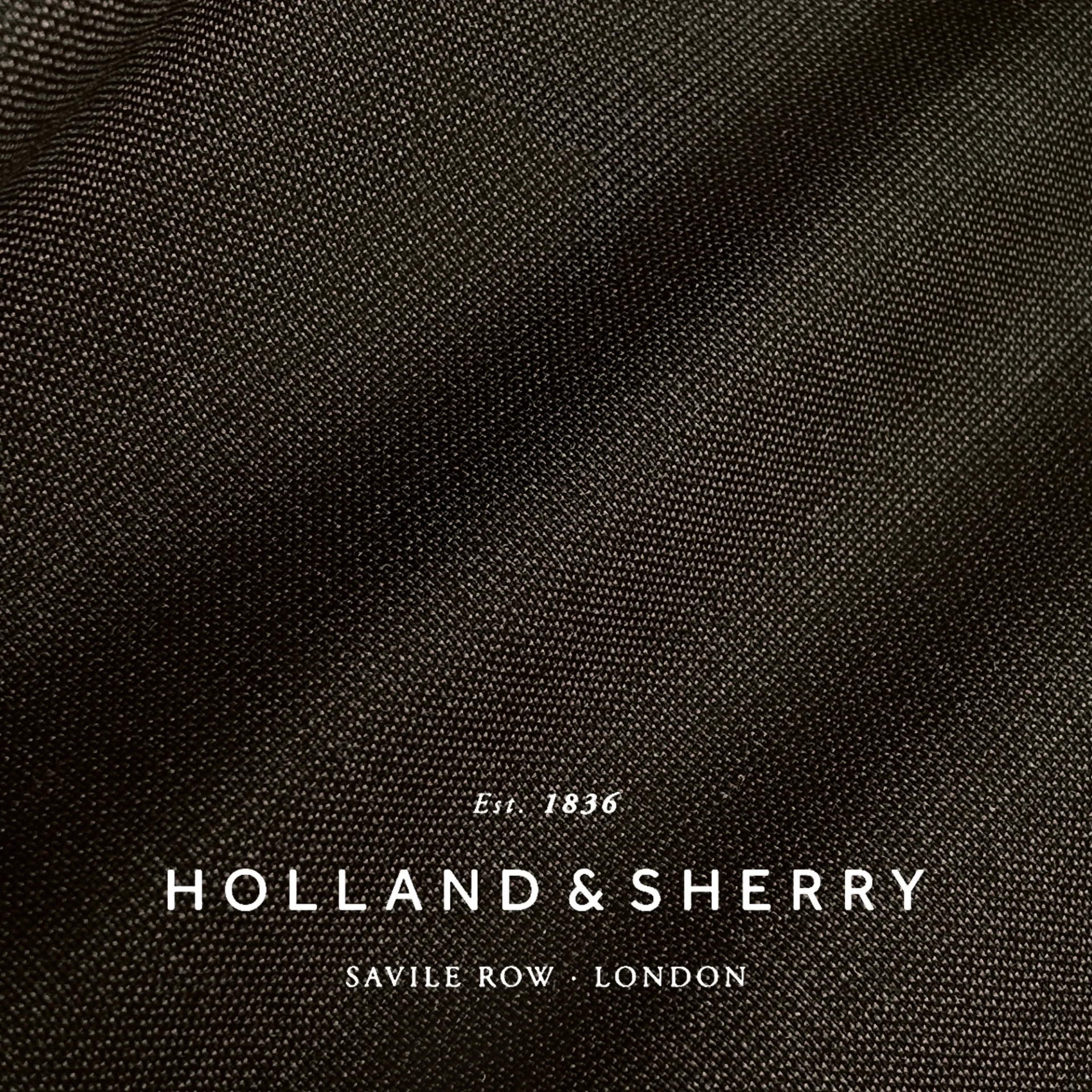 Holland & Sherry black fabric close-up with logo, established 1836, Savile Row, London. Ideal for bespoke tailoring.