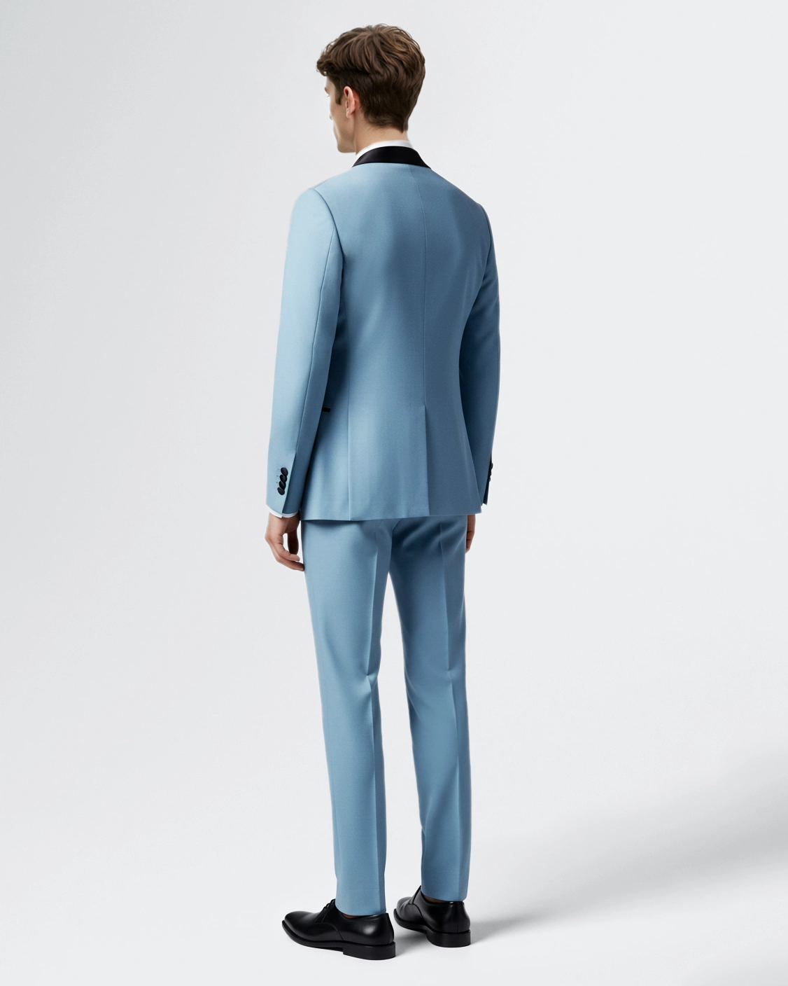 Man in a stylish light blue suit with black lapel, viewed from the back, against a plain background.