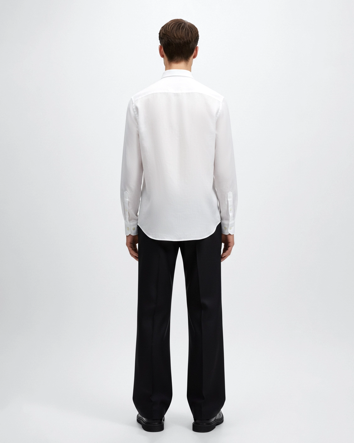 Man in white shirt and black trousers standing with back facing, minimalist fashion.