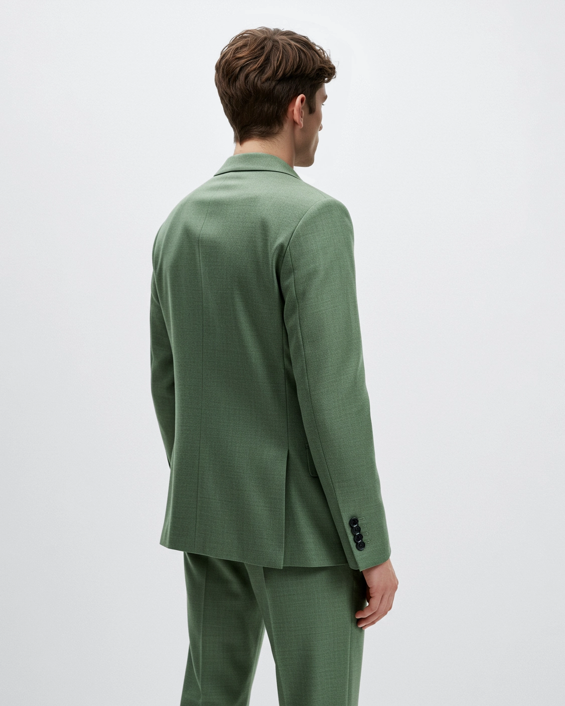 Rear view of a person in a green suit with buttoned sleeves, standing against a plain background.