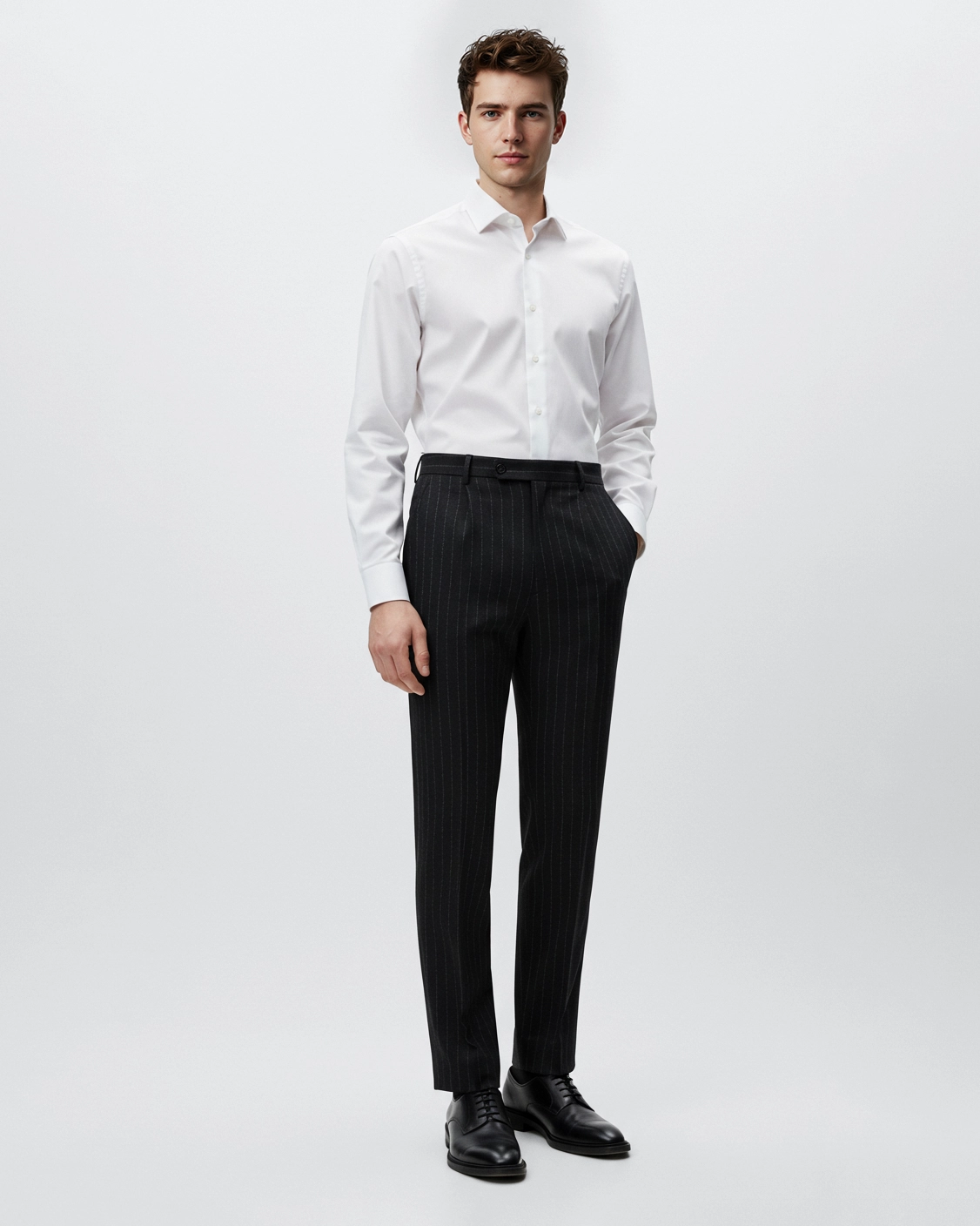 Young man in a white dress shirt and black pinstripe trousers, standing against a plain background.