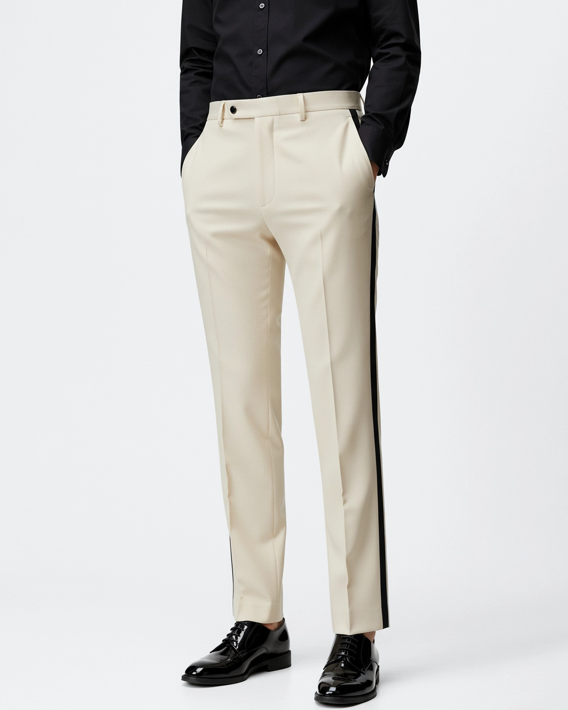 Man in beige dress pants with black side stripe and black shirt, wearing black polished shoes, hands in pockets.