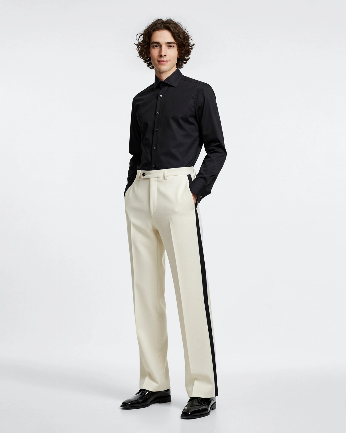 Young man in stylish black shirt and white trousers with black stripe, standing confidently against a plain background.