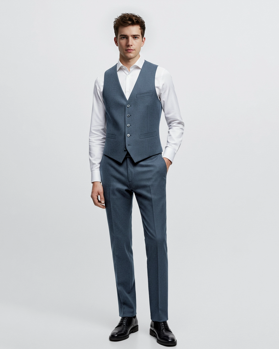 Man in stylish blue suit vest and trousers with white shirt, standing confidently against white background.