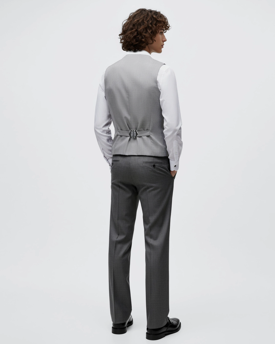 Man in a gray suit and white shirt, viewed from the back, standing against a white background.