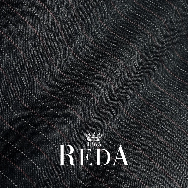 Close-up of dark pinstripe fabric with REDA 1865 logo, showcasing premium textile quality.