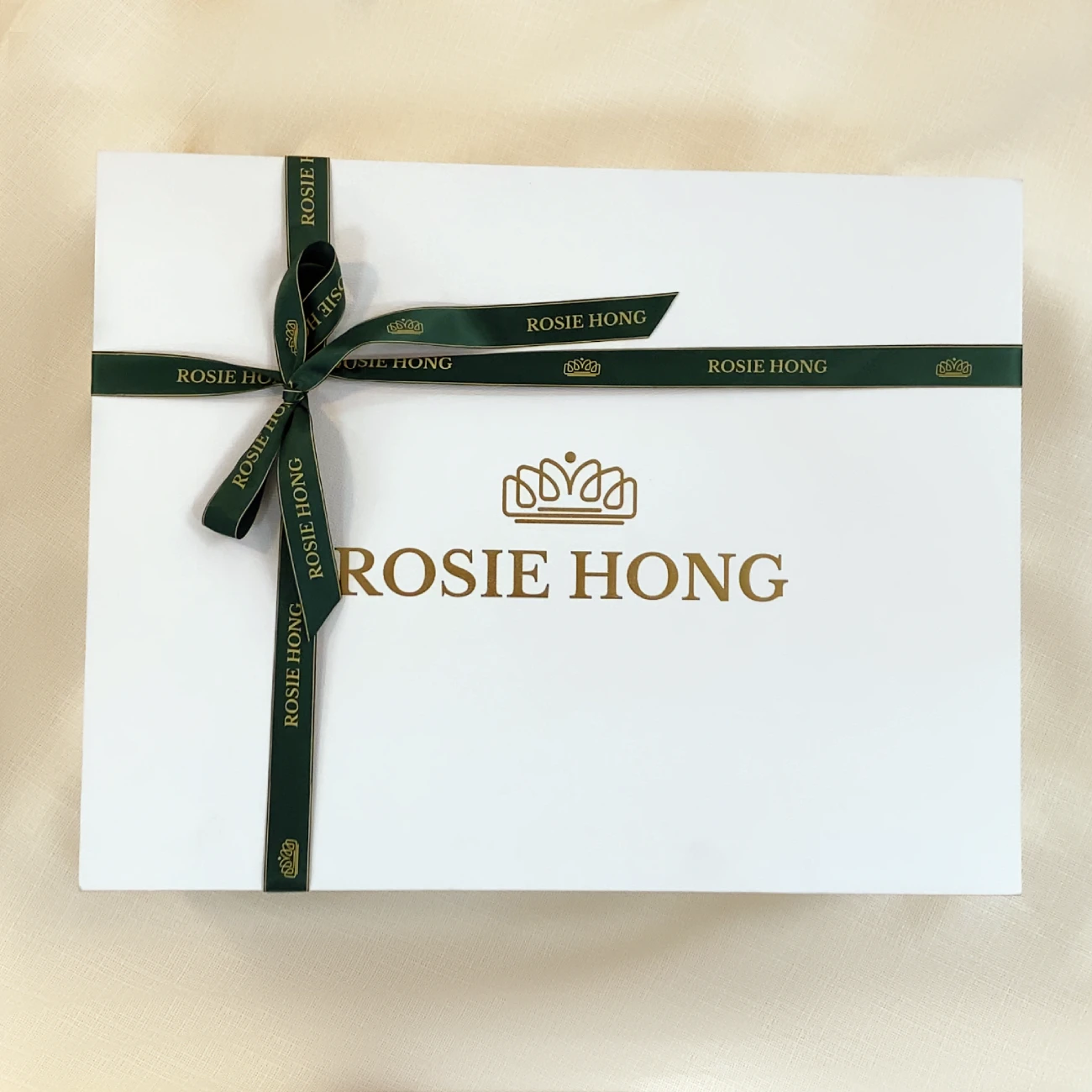 Elegant gift box with a green ribbon, featuring ROSIE HONG branding and crown logo on a sleek white surface.