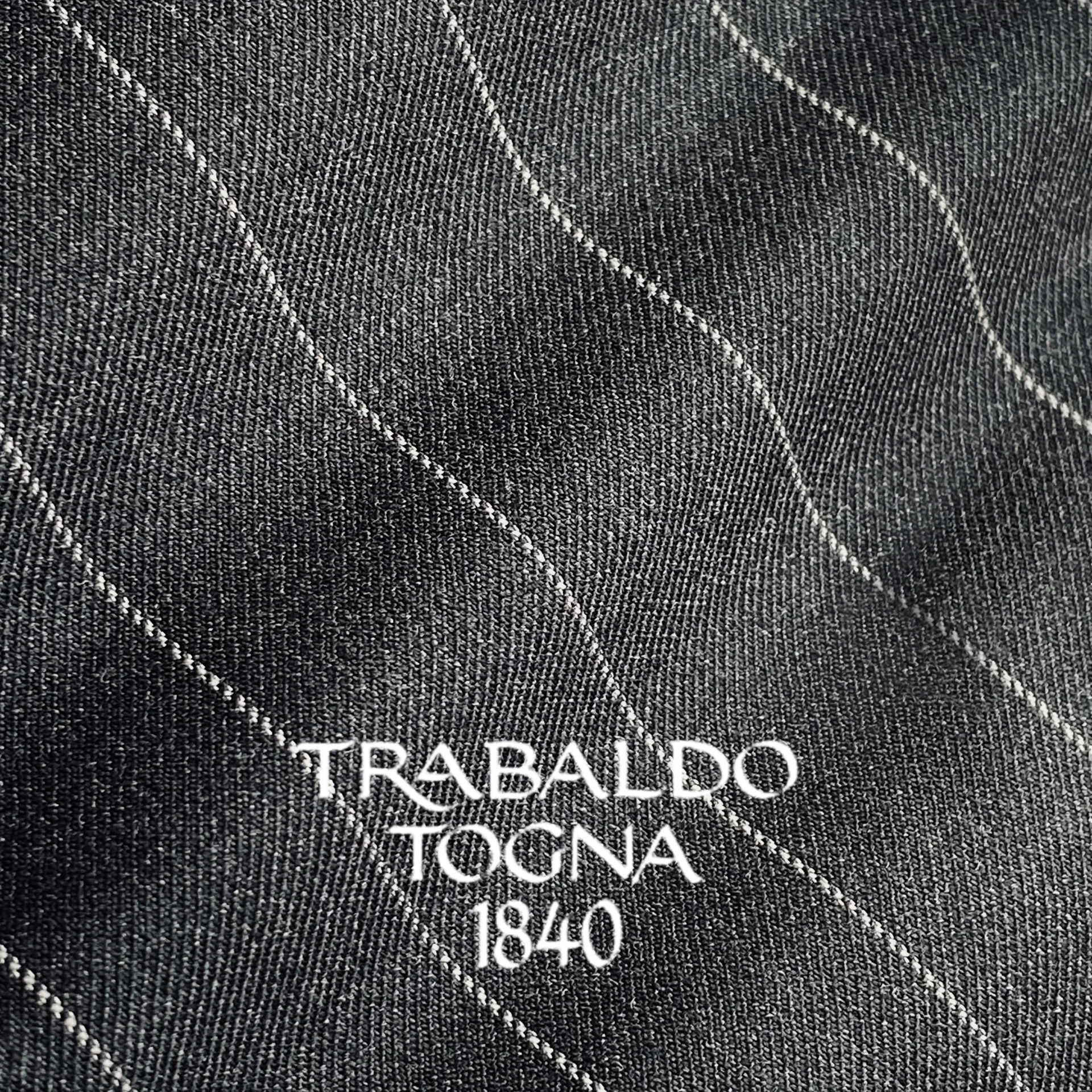 Close-up of textured black fabric with white diagonal lines and TRABALDO TOGNA 1840 text.