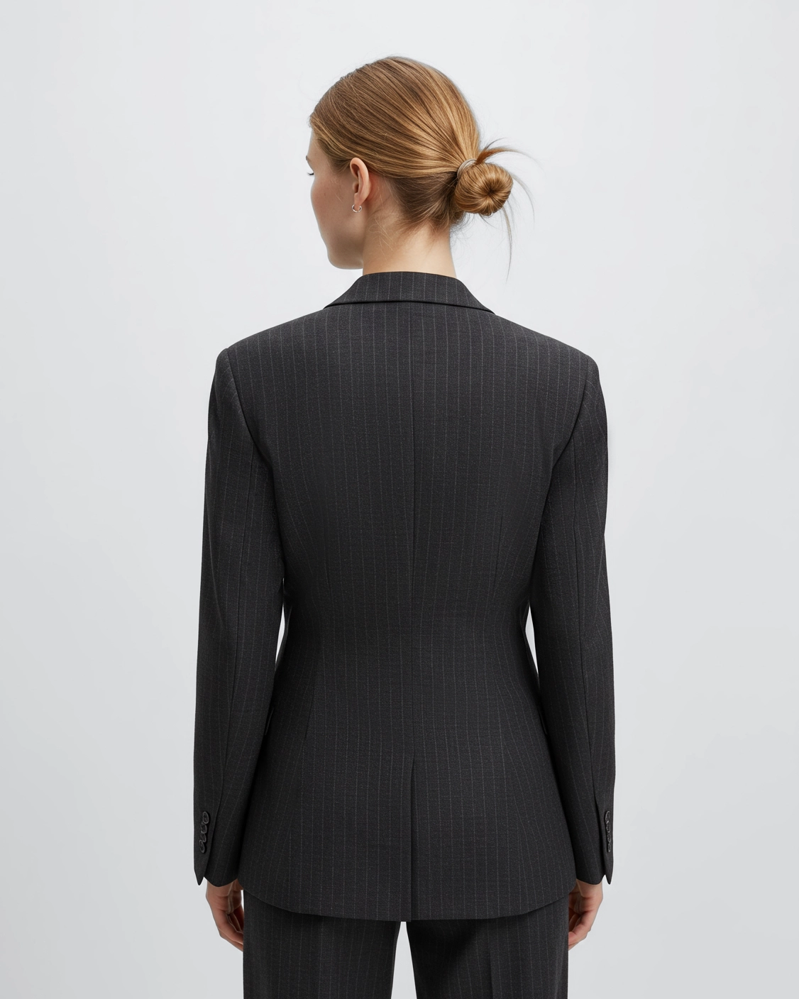 Rear view of a woman in a pinstripe suit jacket with hair in a bun, against a plain background.