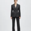 Woman in a tailored dark pinstripe suit standing against a white background.