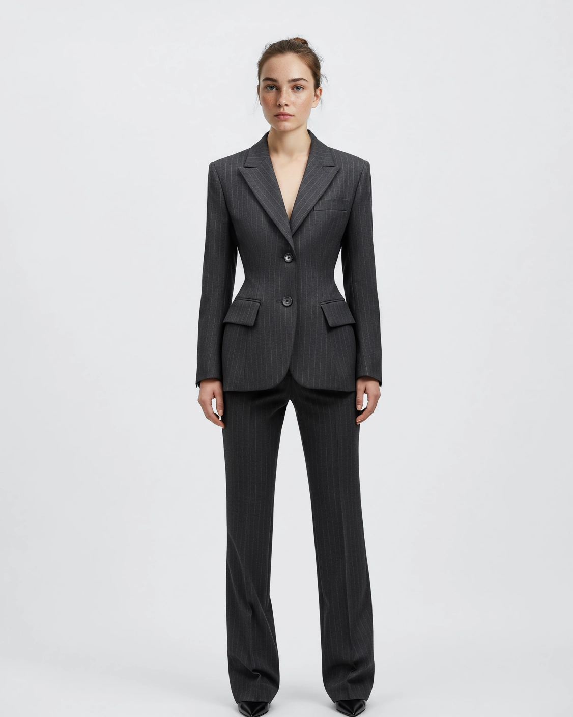 Woman in a tailored dark pinstripe suit standing against a white background.