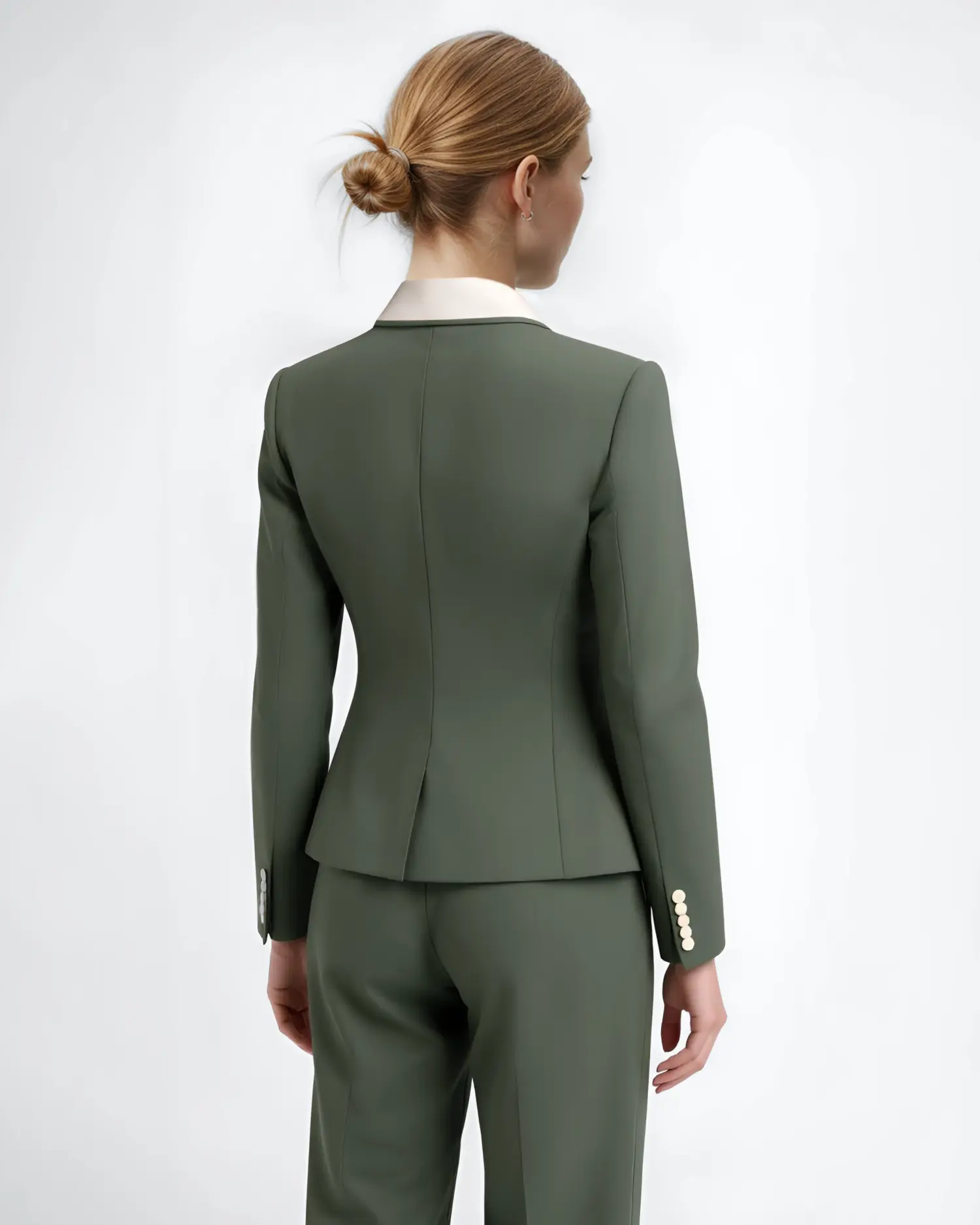 Woman in green suit with a bun hairstyle, viewed from behind, standing against a white background.