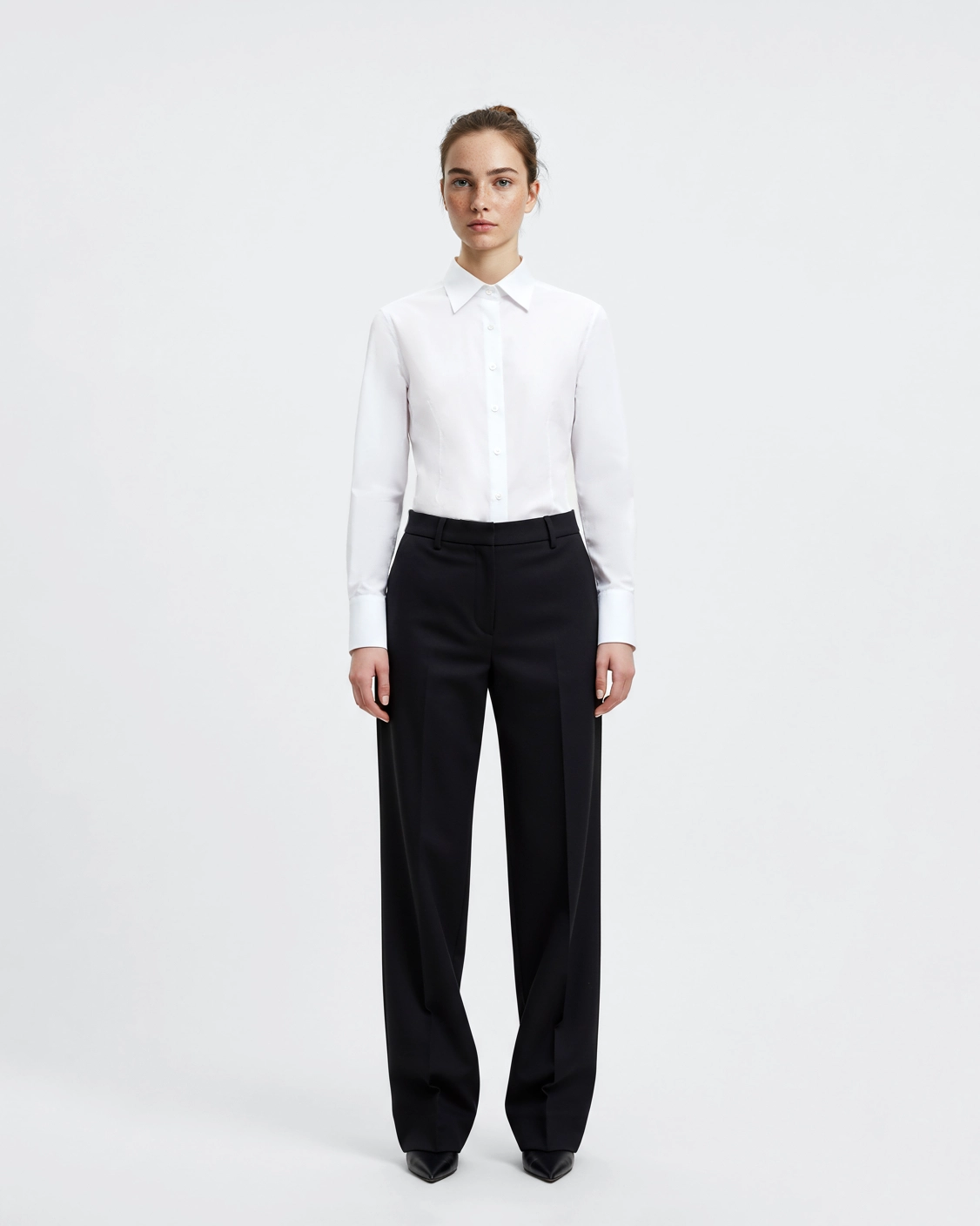 Person wearing a white button-up shirt and black tailored pants against a plain background.