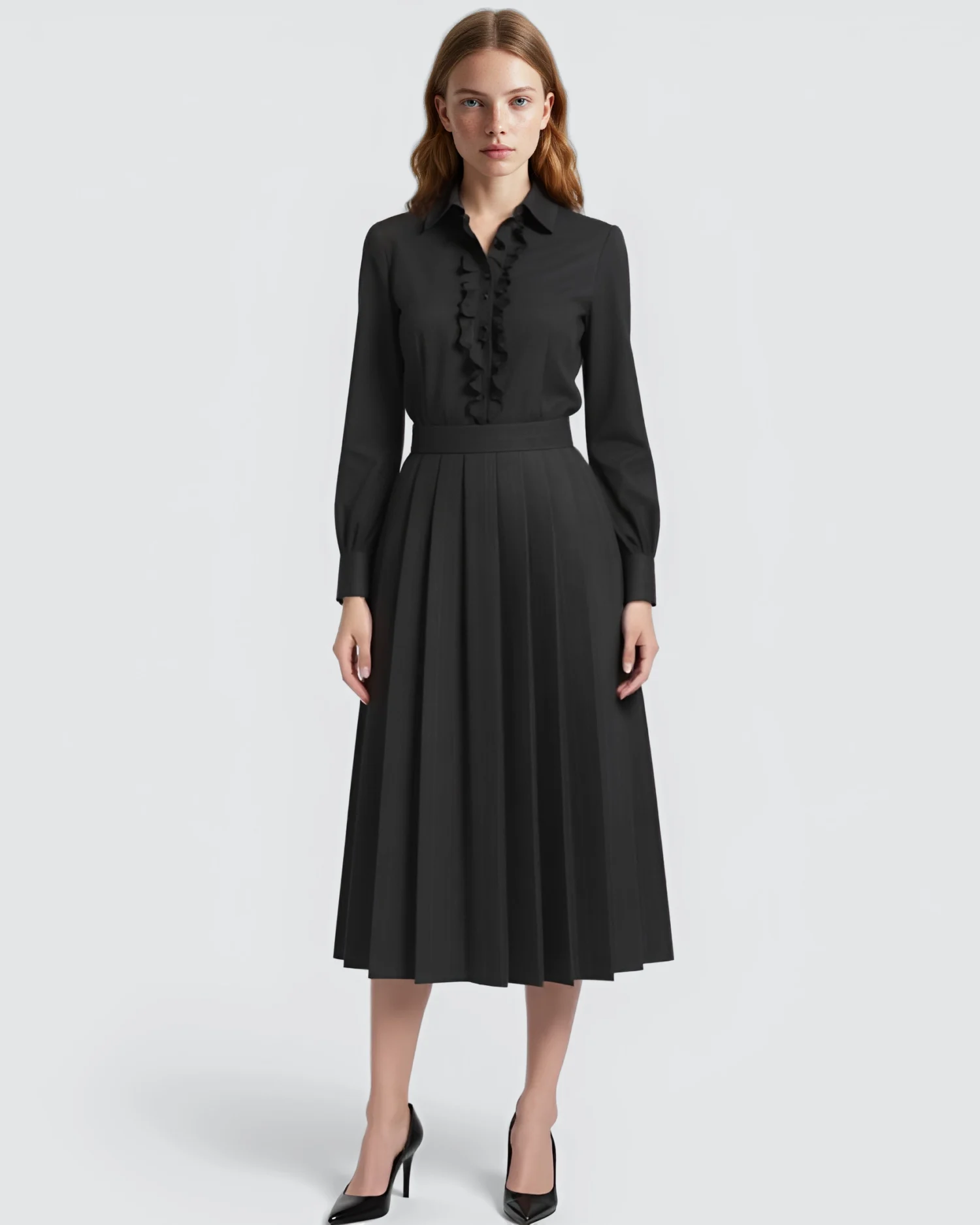 Woman in elegant black midi dress with ruffled details and pleated skirt, standing against a white background.