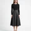 Woman in black top and gray pinstripe skirt stands against white background. Fashion, elegance, modern style.