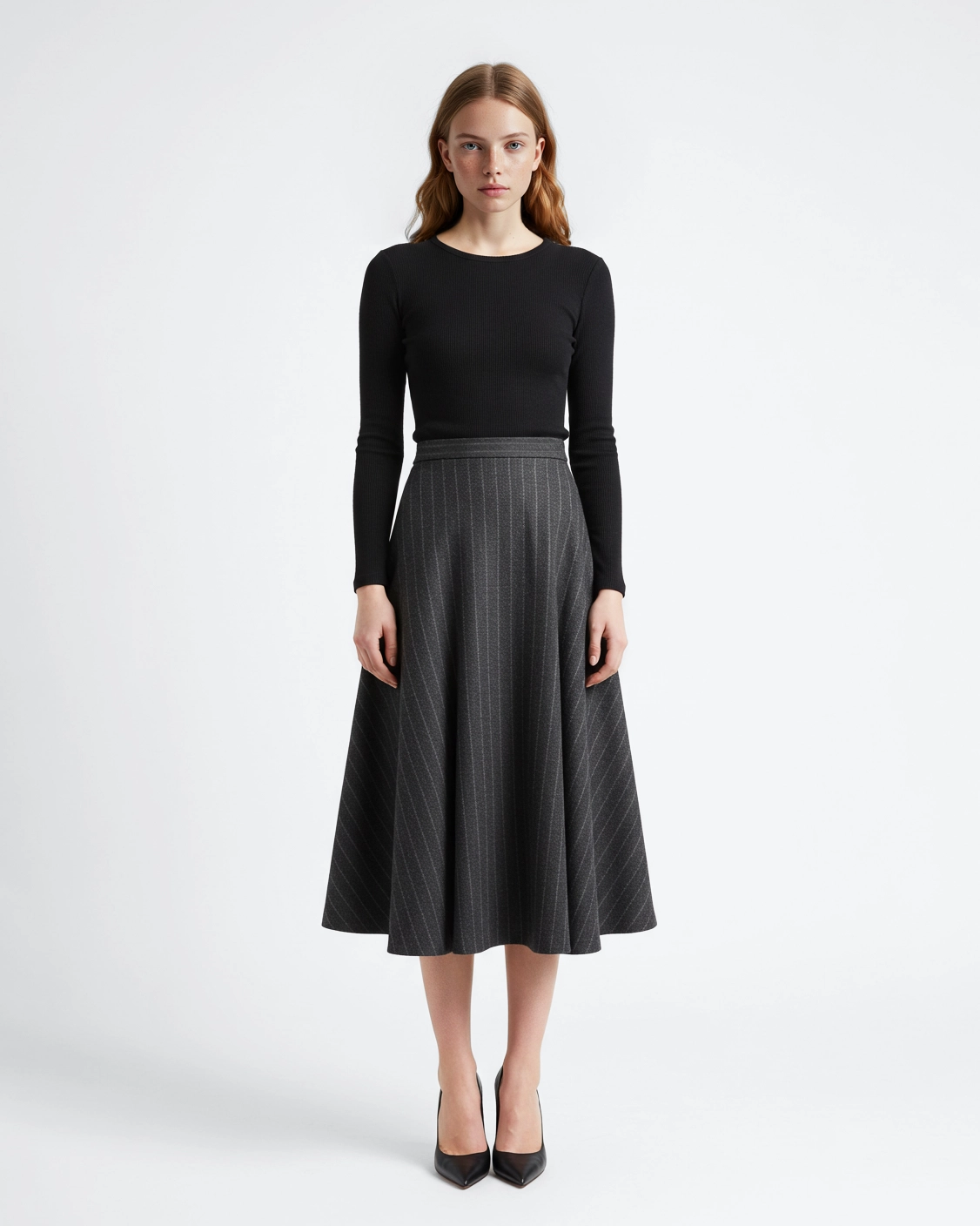Woman in black top and gray pinstripe skirt stands against white background. Fashion, elegance, modern style.