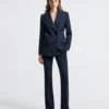 Woman in stylish dark blue suit standing against white background.