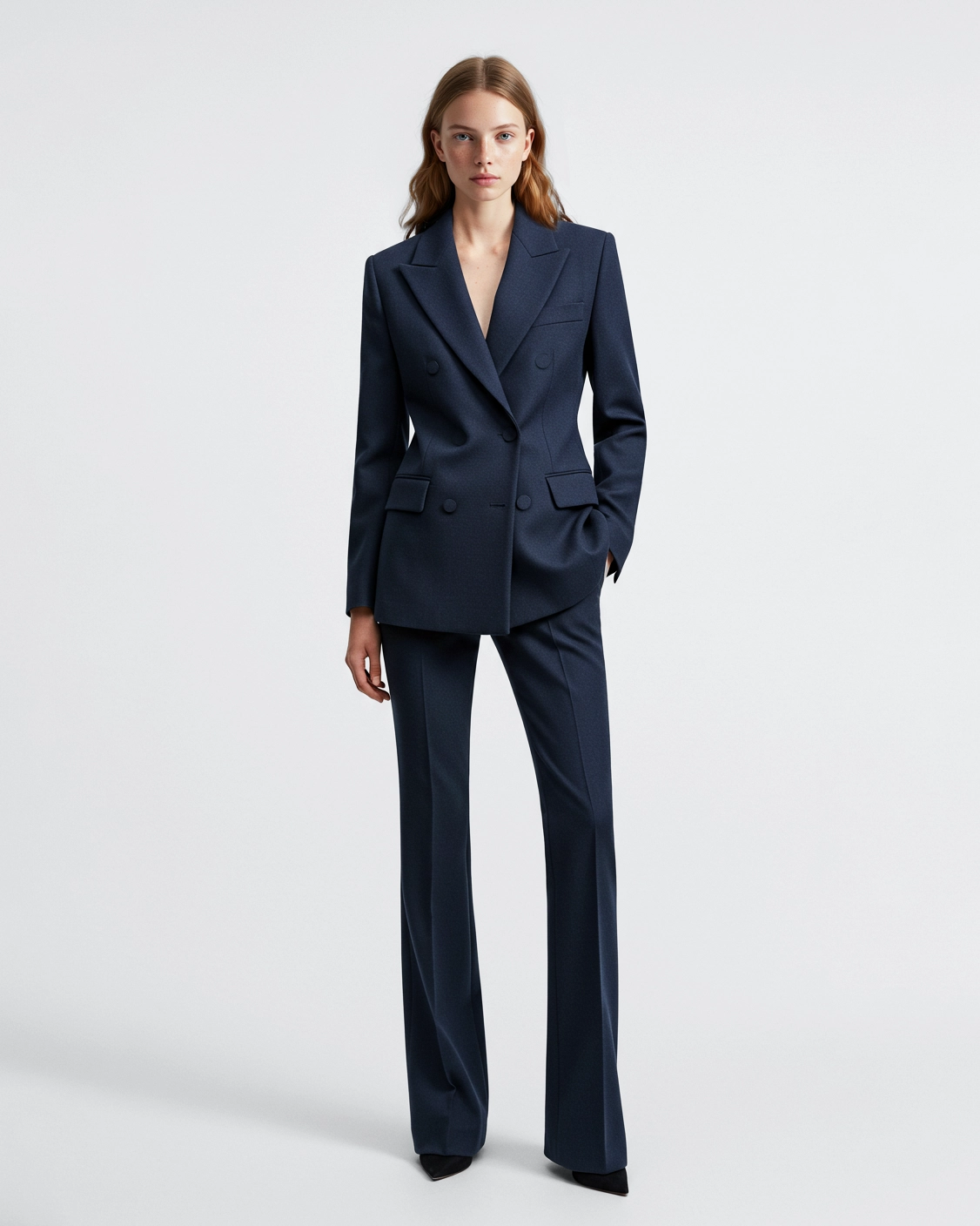Woman in stylish dark blue suit standing against white background.